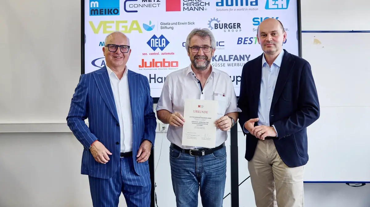 sutter-robotiktag-urkundenübergabe-2025.jpg Drei Männer bei einer Urkundenübergabe vor einer Sponsorenwand am Robotiktag 2025; ein Vertreter von Sutter Medizintechnik hält die Urkunde der Hochschule Offenburg.