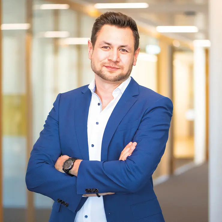 Ein Mitarbeiter von Sutter Medizintechnik steht mit verschränkten Armen im Büroflur und trägt ein blaues Sakko über einem weißen Hemd.