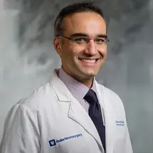 Prof. Zomorodi in weißem Arztkittel mit Hemd und Krawatte vor grauem Hintergrund.