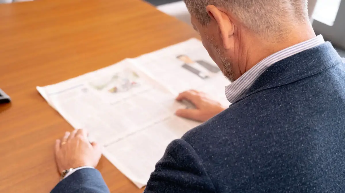 Nahaufnahme eines Mannes im Anzug, der an einem Holztisch sitzt und ein Dokument aufmerksam liest