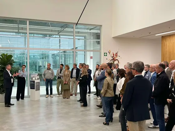 Eine größere Besuchergruppe steht im Foyer und hört einem Vortragenden im modernen Firmengebäude zu.