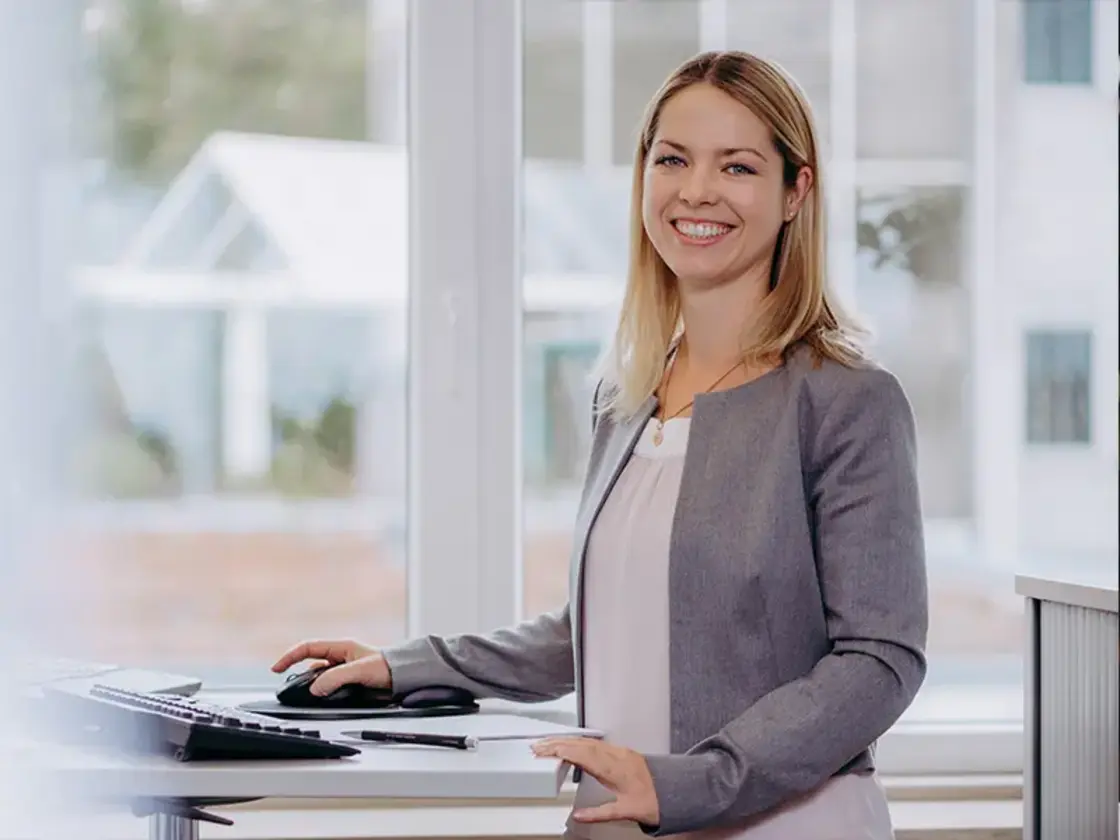mitarbeiterin-office-sutter-medizintechnik.jpg Mitarbeiterin von Sutter Medizintechnik an einem höhenverstellbaren Schreibtisch – modernes Arbeitsumfeld mit Fokus auf Ergonomie