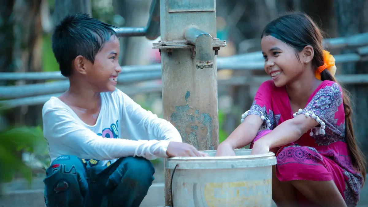 kinder-lachen-wasserpumpe © World Vision.jpg Zwei lachende Kinder waschen sich die Hände an einer Wasserpumpe und genießen den Zugang zu sauberem Wasser in einem ländlichen Dorf.