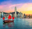 Hongkong_Skyline_Junkboot_Sonnenuntergang Traditionelles chinesisches Junkboot mit roten Segeln fährt vor der Skyline von Hongkong bei farbenprächtigem Sonnenuntergang über das Wasser.