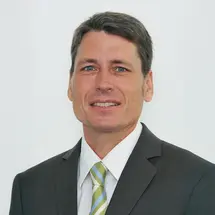 Prof. Gerlach im dunklen Anzug mit gestreifter Krawatte vor hellem Hintergrund.