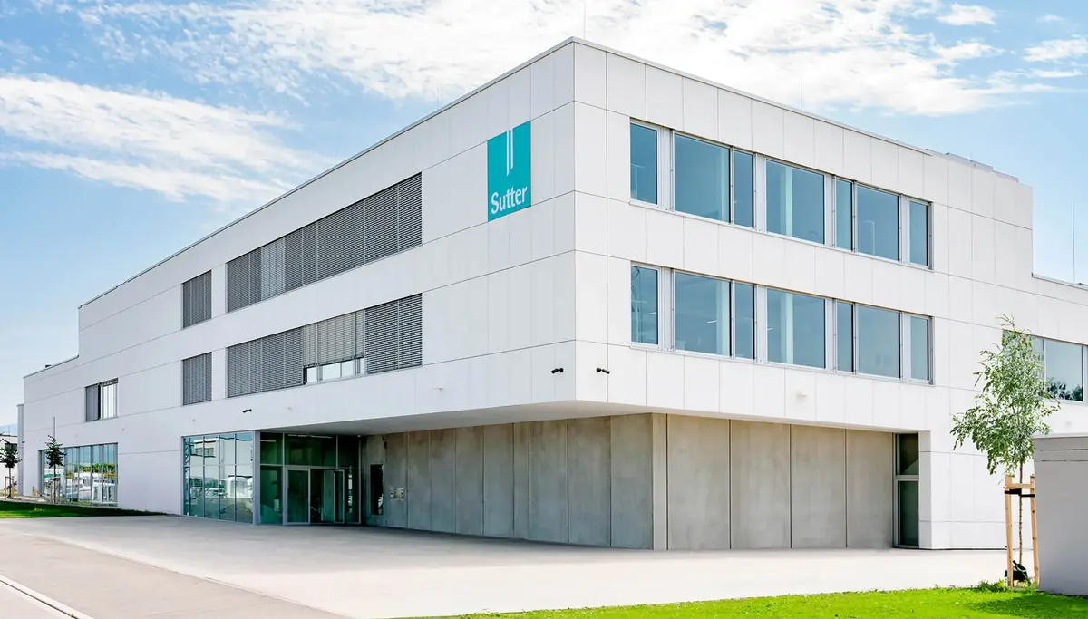 Modernes weißes Gebäude mit großen Fenstern und einzigartigem architektonischem Design. Das zweistöckige Gebäude besitzt ein auskragendes Obergeschoss und geometrische Formen an der Fassade, die den zeitgenössischen Stil unterstreichen.