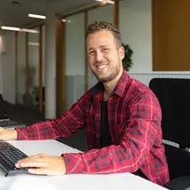 Ein lächelnder Mitarbeiter der IT-Abteilung von Sutter Medizintechnik sitzt entspannt an seinem Schreibtisch im Büro und arbeitet am Computer.