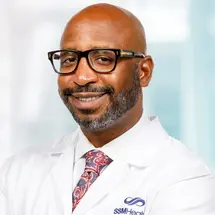 Person in white lab coat with SSM Health logo, wearing glasses and a colorful tie – professional representation in a medical setting.